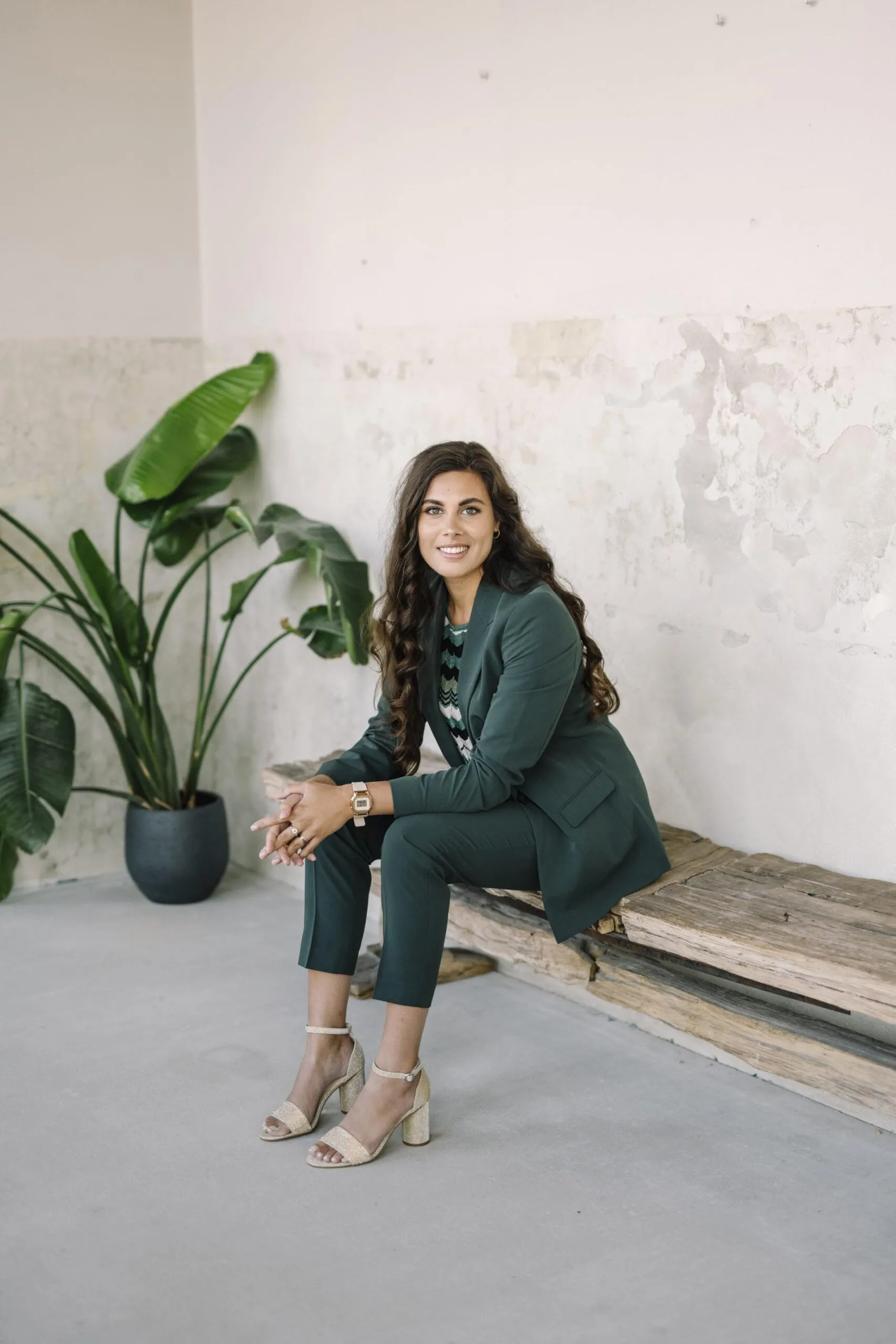 Laura docent interieurstyling op een houten bank voor een kale muur met een plant in de hoek