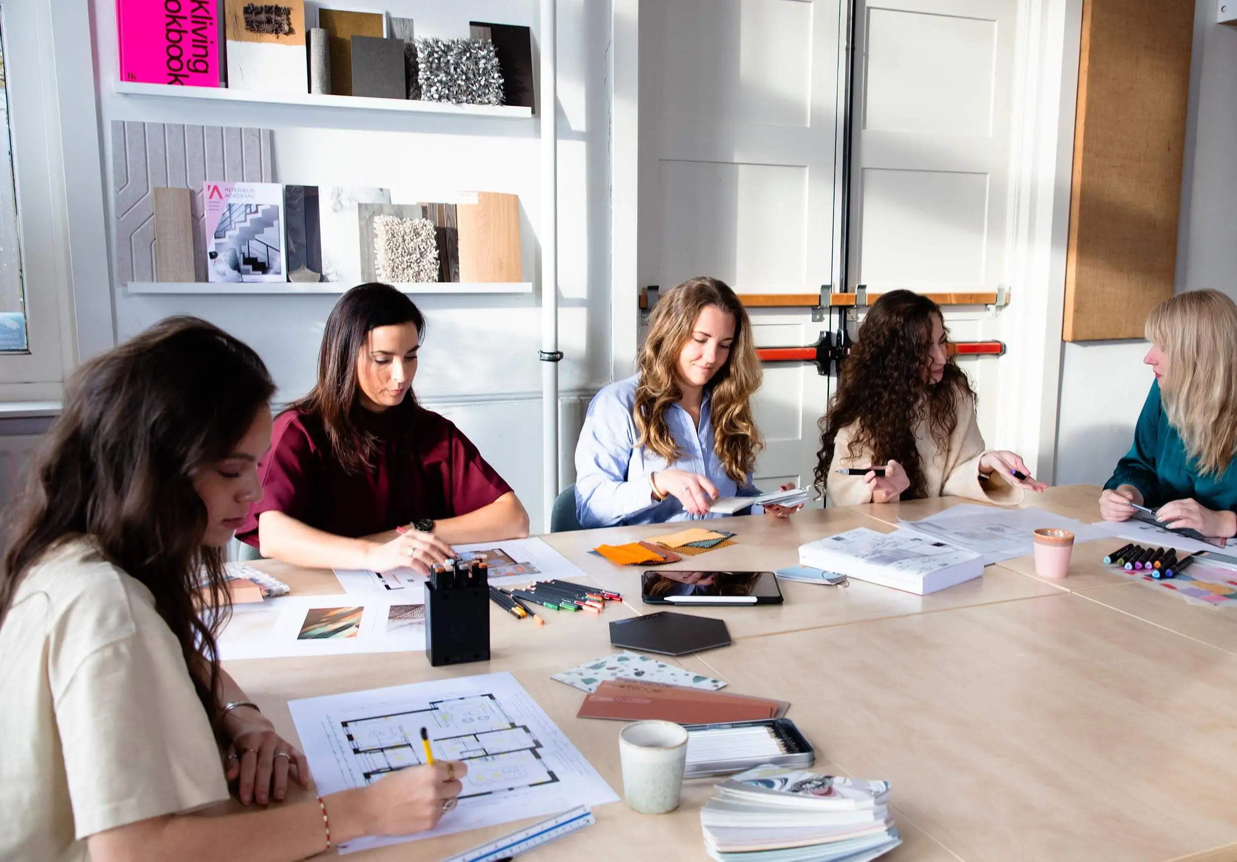 Groep vrouwelijke deelnemers van de cursus interieurontwerper aan tafel, bezig met het uitwerken van opdrachten