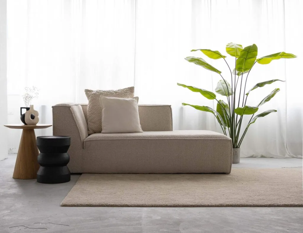 Stoffen bank met bijzettafels en grote groene plant op laagpolig vloerkleed gestyled voor interieurfotografie opleiding.